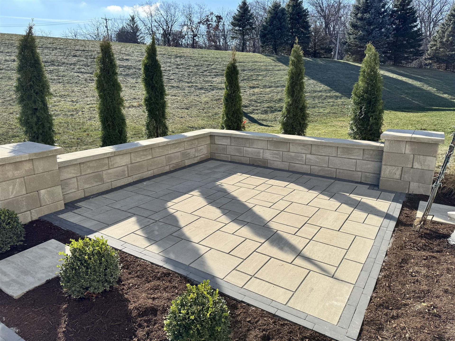 Paver patio with seat wall and evergreen privacy trees built by Yuritzy Landscape